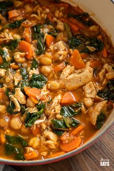a bowl filled with chicken, carrots and spinach soup on top of a wooden table