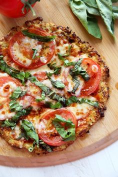 a pizza with tomatoes, basil and cheese on a cutting board