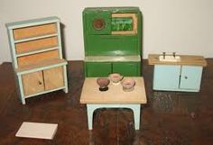several toy furniture including a green stove, sink and table with dishes on it sitting on a wooden floor