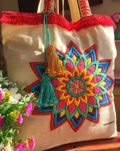 an embroidered bag with tassels and flowers in the background