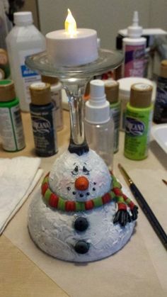 a snowman candle holder sitting on top of a table next to bottles and paint