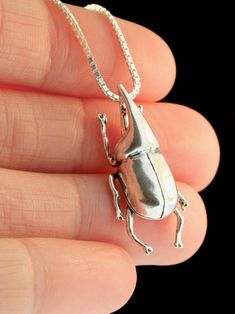 a small silver frog necklace on a person's hand