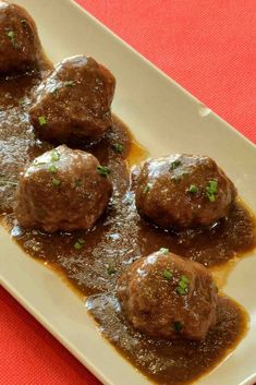 meatballs covered in gravy sit on a white plate with red cloth underneath