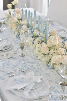 a long table is set with white and blue floral centerpieces, silverware, and candles