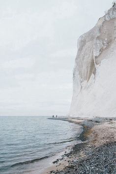 two people standing on the beach next to some white cliffs