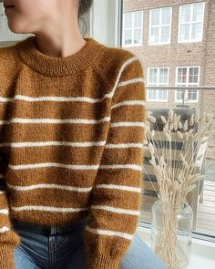 a woman sitting on a window sill wearing a brown and white striped knit sweater
