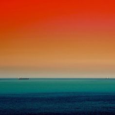 an orange and blue sky over the ocean with boats in the distance on the horizon