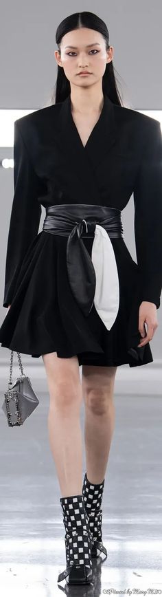 a woman is walking down the runway in a black dress