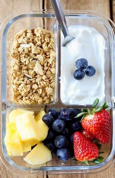 a plastic container filled with yogurt, fruit and granola on top of a wooden table