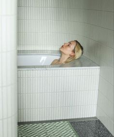 a woman laying in a bathtub with her head above the edge and eyes closed