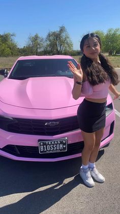 a woman standing in front of a pink car with her hands out to the side