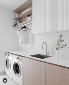 a washer and dryer in a white laundry room with wooden cabinets, hanging clothes on the wall