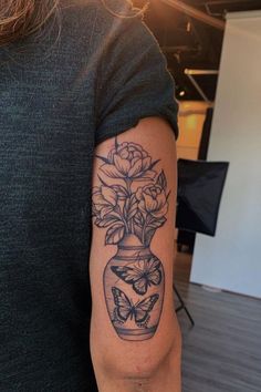 a woman with a tattoo on her arm holding a vase filled with flowers and butterflies