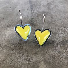 two yellow and blue heart shaped earrings sitting on top of a cement floor next to each other