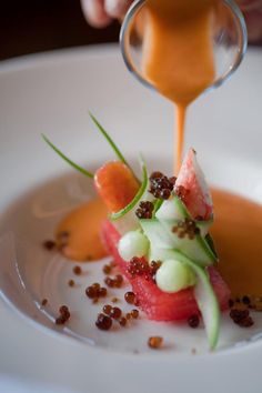 a person pouring sauce onto a plate with food on it and garnishes