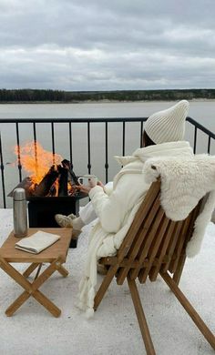 a person sitting in a chair next to a fire on top of a snow covered ground