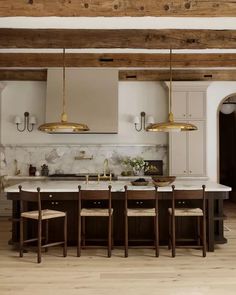 a large kitchen with marble counter tops and gold pendant lights hanging from the wooden beams