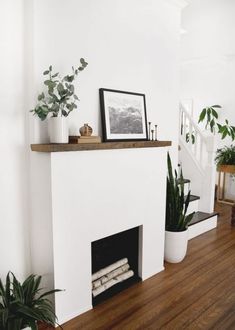 a white fireplace with plants and pictures on the mantle
