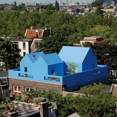 an aerial view of a blue house with trees in the foreground and buildings in the background