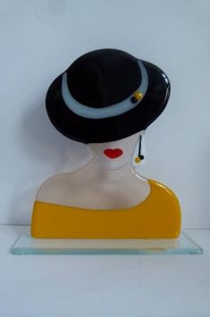 a glass figurine with a black hat on it's head and yellow base