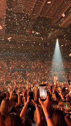 a large crowd at a concert with confetti falling from the ceiling and people holding up their cell phones
