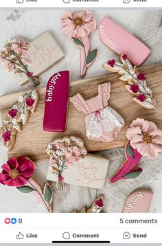 some pink and white cookies are on a wooden board with flowers, leaves and other decorations