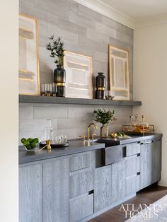 a kitchen with two sinks and some framed pictures on the wall above it, along with gold accents