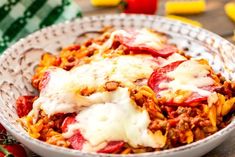 a bowl filled with pasta and meat covered in sauce, cheese and tomato slices on top