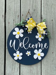 a welcome sign hanging on the side of a wooden fence with daisies around it