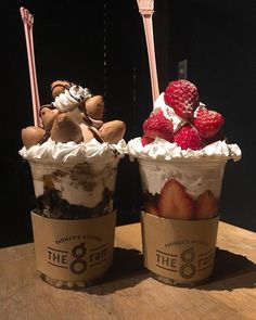 two ice cream sundaes with strawberries and whipped cream on top sitting on a table