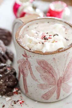 hot chocolate and marshmallows in a mug next to cookies on a table