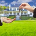 two people handing keys to each other in front of a house