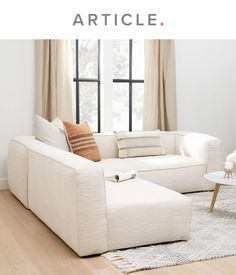 a living room with white couches and pillows on the floor next to a window