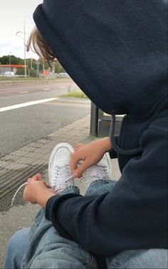 a person in a hoodie sitting on the ground with their feet crossed and one hand holding a cell phone