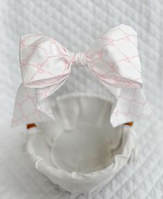 a white bowl with a pink and white bow tie on the top, sitting on a bed