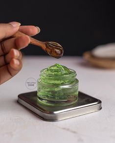 a hand holding a wooden spoon over a jar filled with green liquid