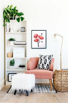 a living room with a pink chair and white bookshelf filled with plants on top of it