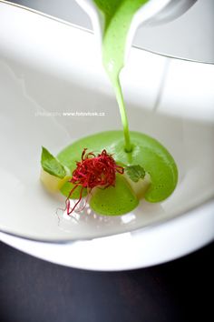 a green substance being poured onto a white plate with red sprouts on it
