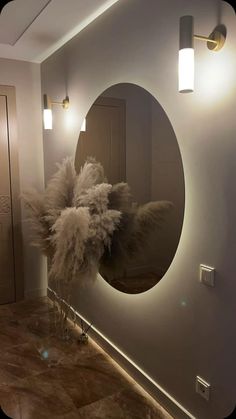 a bathroom with a round mirror and lights on the wall next to a vase filled with dry grass
