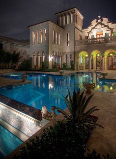 a large house with a swimming pool in the middle of it at night, surrounded by greenery