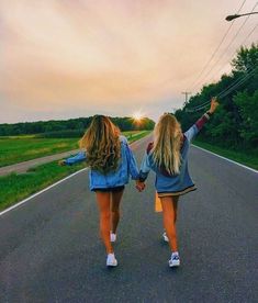 two girls walking down the road holding hands and waving at the sun in the distance