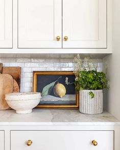 a kitchen with white cabinets and marble counter tops, including a painting on the wall