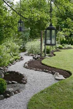 a garden with gravel and rocks in the grass, trees and lanterns hanging over it