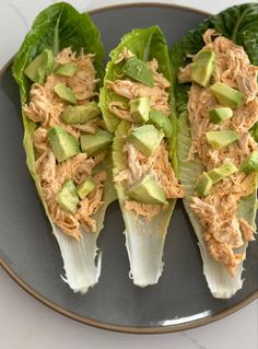 three lettuce wraps with shredded chicken and avocado on top, sitting on a black plate