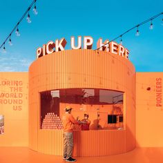 a man standing in front of an orange building with the words pick up here on it
