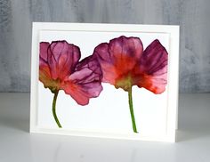 three pink flowers on a white card with watercolor paint and paper in the middle