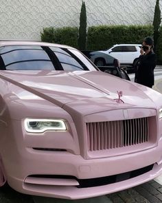 a pink rolls royce parked on the side of a road next to a man in a black jacket