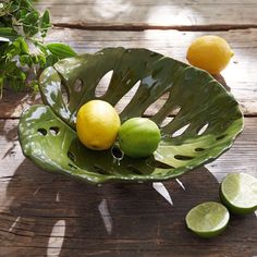 two lemons and one lime in a green bowl on a wooden table with leaves