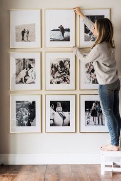 a woman standing on a step stool in front of a wall with many pictures hanging on it