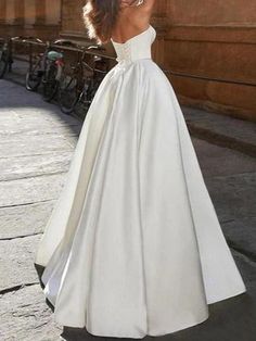 a woman in a white wedding dress standing on the street with her back to the camera